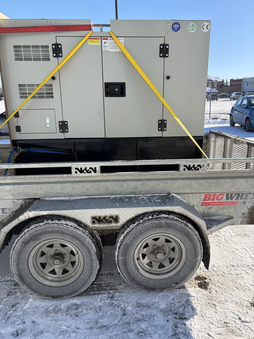 Génératrice grise sanglée sur une remorque, avec de la neige au sol